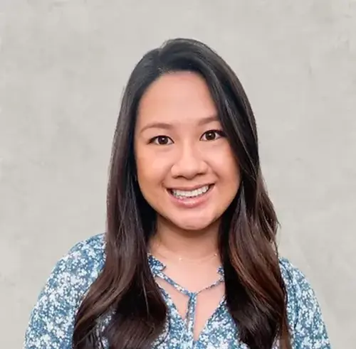 Smiling woman with long dark hair wearing blue patterned top against neutral background.