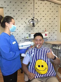 Dental professional in blue scrubs examines young patient wearing striped bib in modern pediatric dental office.