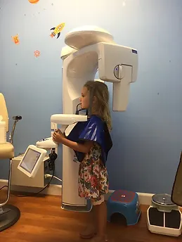 Young child operating dental imaging equipment in pediatric dental office setting.