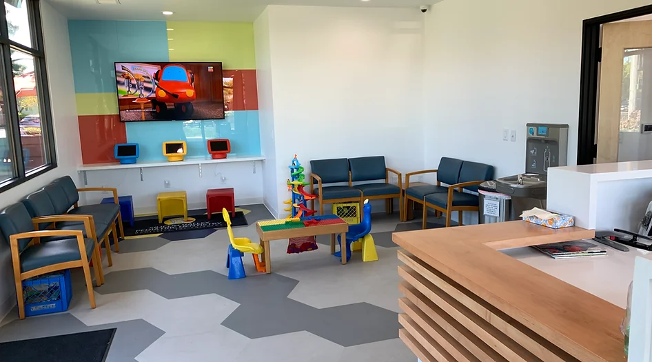 Colorful pediatric dental office playroom with toys, seating areas, and child-friendly furnishings.