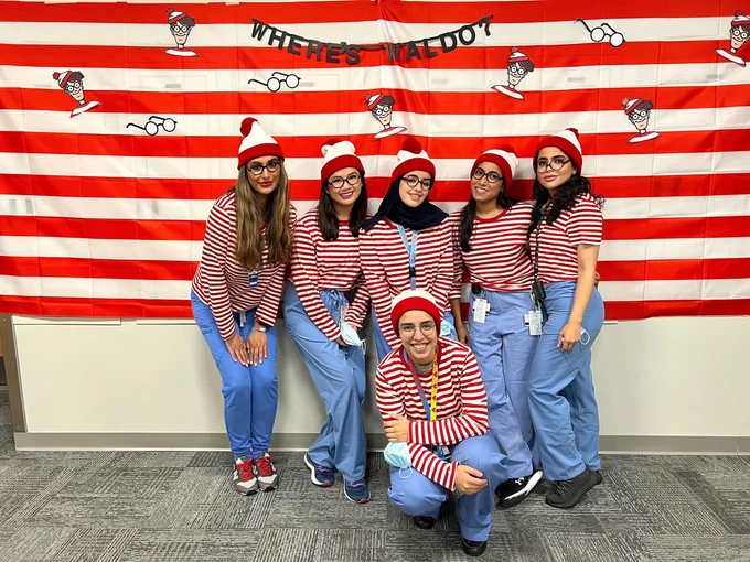 Six people in red and white striped outfits posing together against red striped background.