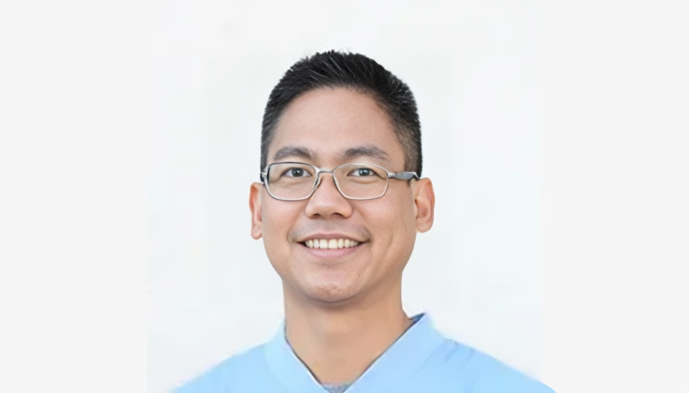 Asian male wearing glasses and light blue shirt smiling against white background