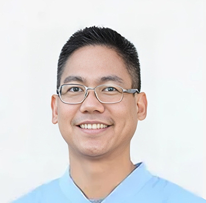 Asian male wearing glasses and light blue shirt smiling at camera, professional headshot