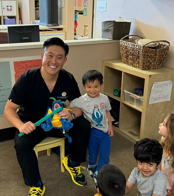 Pediatric dentist playing with colorful toy with young children in dental office playroom.