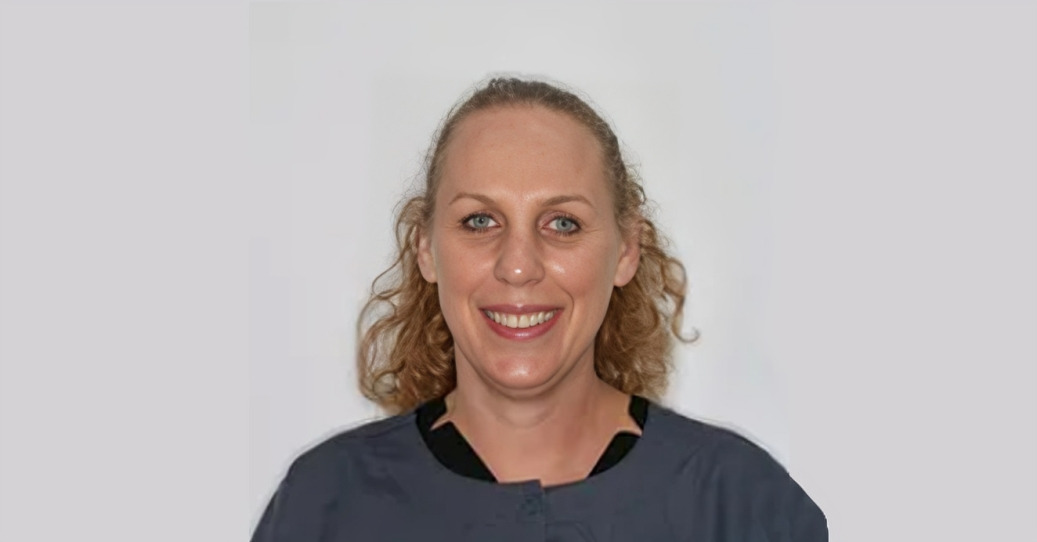 Professional headshot of smiling woman with wavy blonde hair against neutral gray background.
