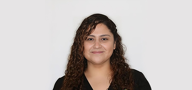 Woman with long dark curly hair wearing black shirt against white background, professional headshot.