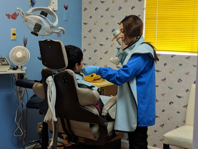 Pediatric dentist in blue coat examining young patient in dental chair in modern clinic.