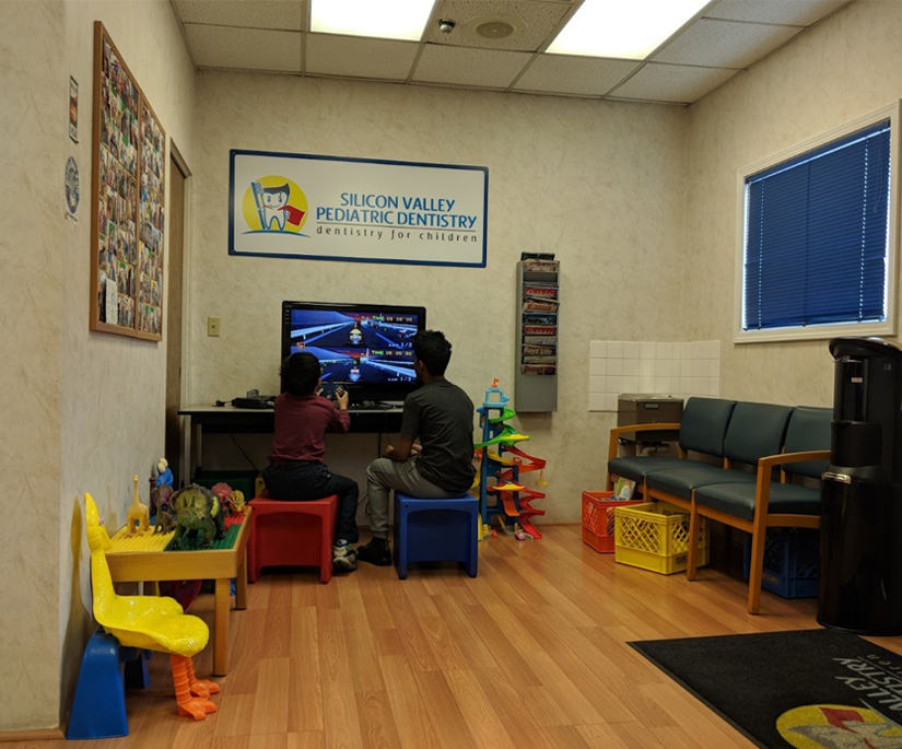 Colorful pediatric dental office playroom with toys, furniture, and entertainment for children patients.