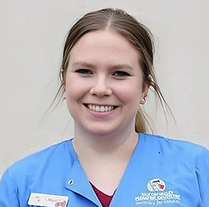 Young female dental professional smiling in blue scrubs against white background.
