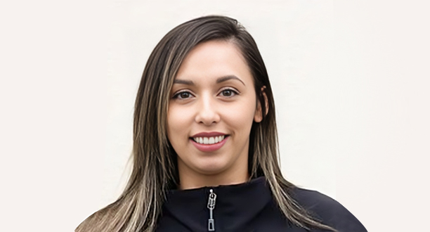 Professional headshot of smiling woman with long dark hair wearing black jacket against white background.