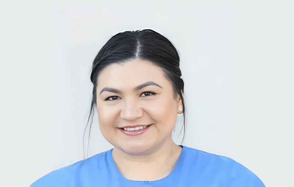 Woman in blue scrubs smiling at camera against white background, dental professional headshot.