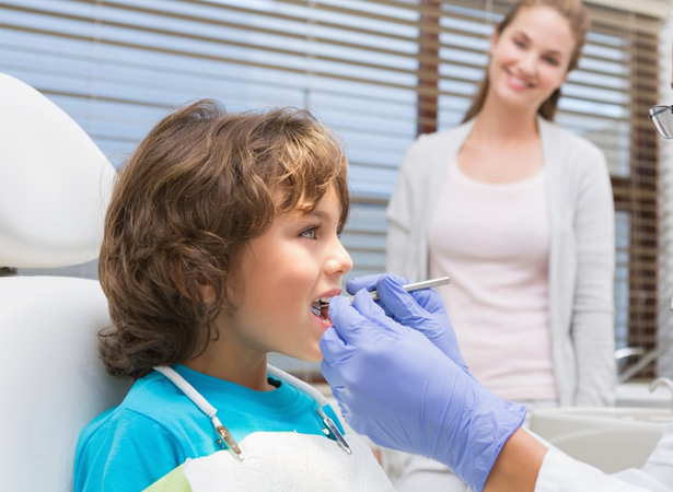 Young boy receiving dental examination from gloved dentist in clinical setting with parent observing.