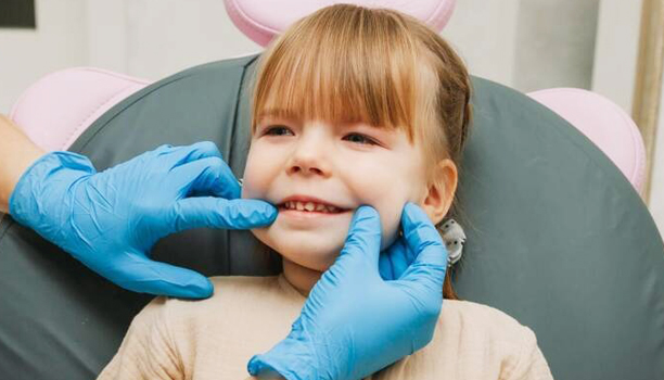 Young child smiling during dental examination with dentist wearing blue gloves in clinical setting.