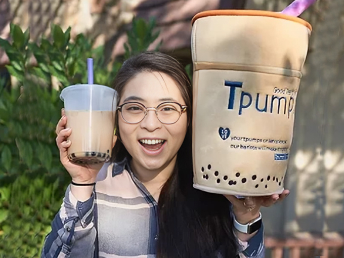 Woman holding large bubble tea drink and promotional cup outdoors in sunny garden setting.