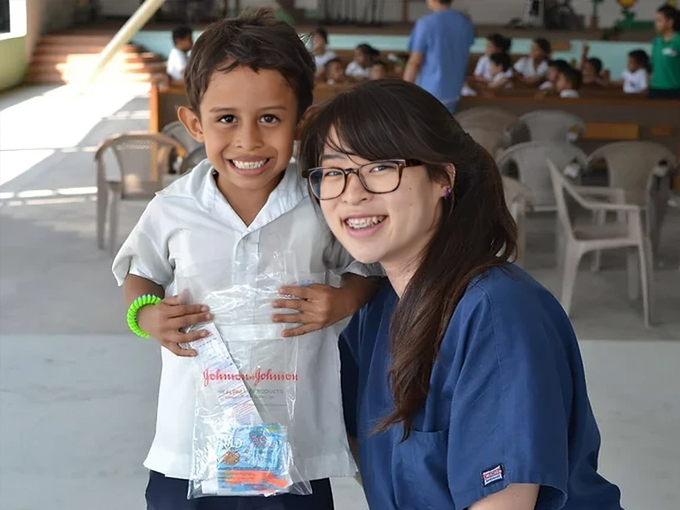 Young child and female dental professional smiling together at pediatric dental office outdoor area.