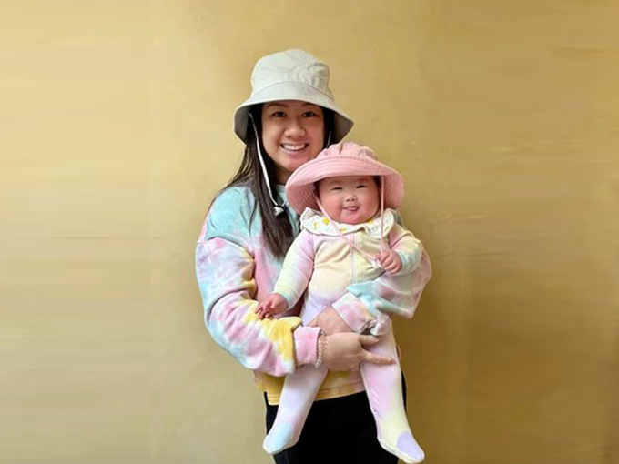 Woman and child wearing matching tie-dye outfits and white bucket hats against yellow background.