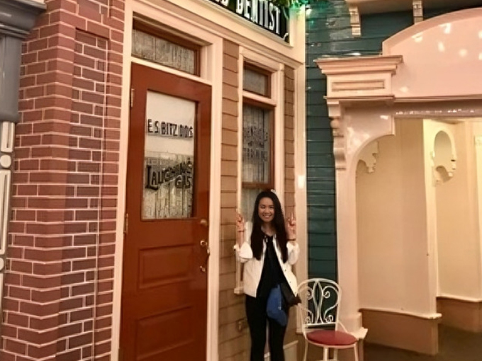 Woman standing in front of red door of dental office entrance with brick and beige walls.