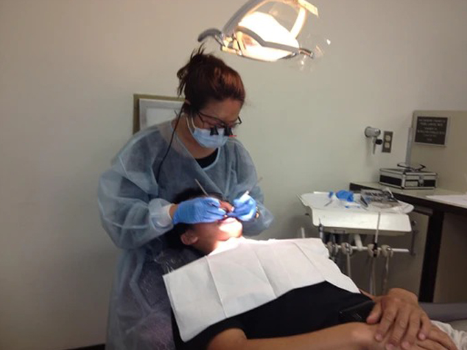 Pediatric dentist examining young patient's teeth in clinical treatment room with overhead light.