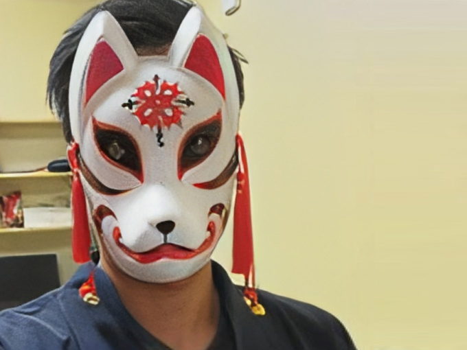 Person wearing red and white Japanese fox mask in dental office setting.