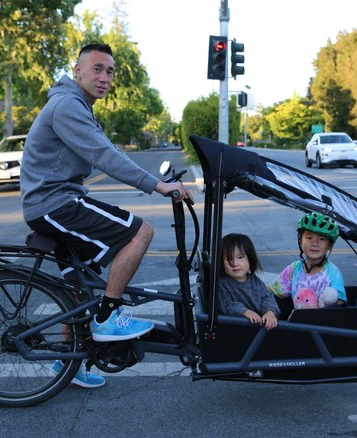 Adult and two children with bicycle and cargo bike at street intersection with traffic light.