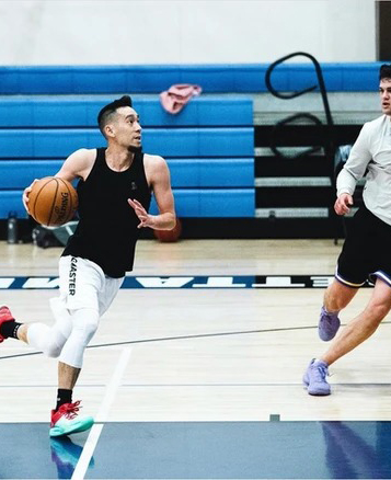 Young athlete dribbling basketball during indoor gym practice with blue bleachers in background.