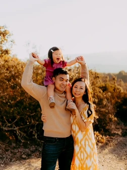 Happy family of four smiling outdoors in golden field at sunset.