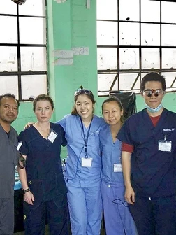Five dental professionals in scrubs and ID badges pose together in a clinical treatment room.