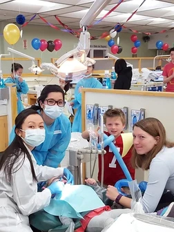 Pediatric dental team treating young patient in colorful clinic room with balloons and decorations.