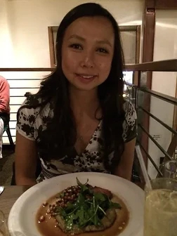 Woman smiling at table with plated food in restaurant or dining setting.