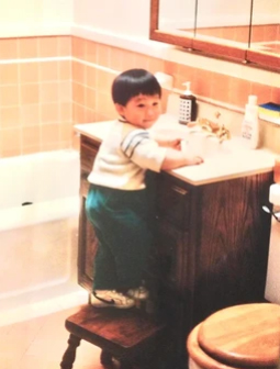 Young child standing on stool at bathroom sink, washing hands or brushing teeth.
