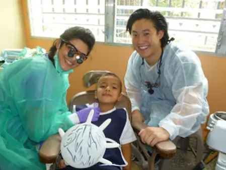 Two dental professionals in scrubs pose with a young child patient in a dental office setting.