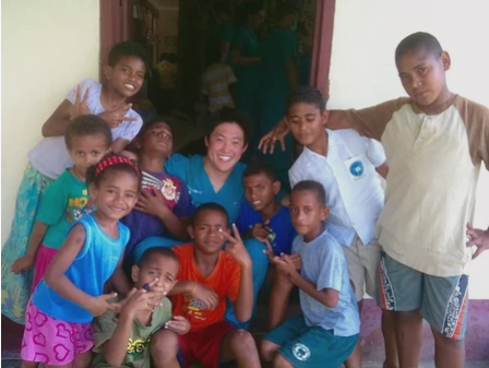 Group of smiling children and adults posing together indoors for a community photo.