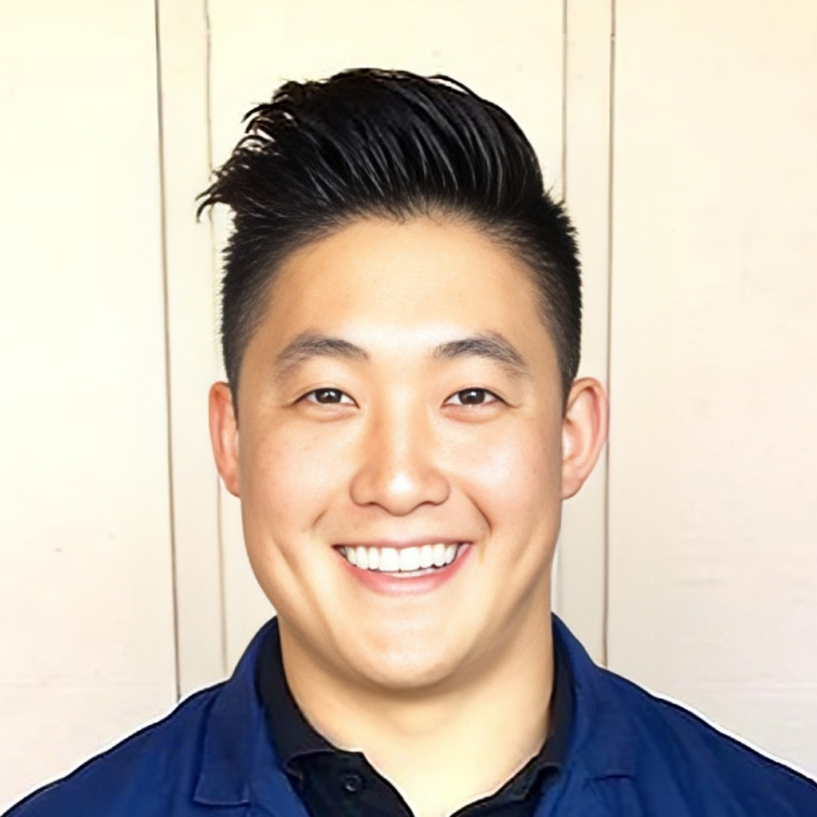 Professional headshot of smiling male dental professional wearing navy blue shirt against neutral background.