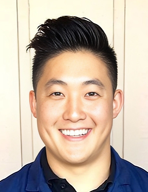 Professional headshot of smiling male dental professional wearing dark blue shirt against white background.
