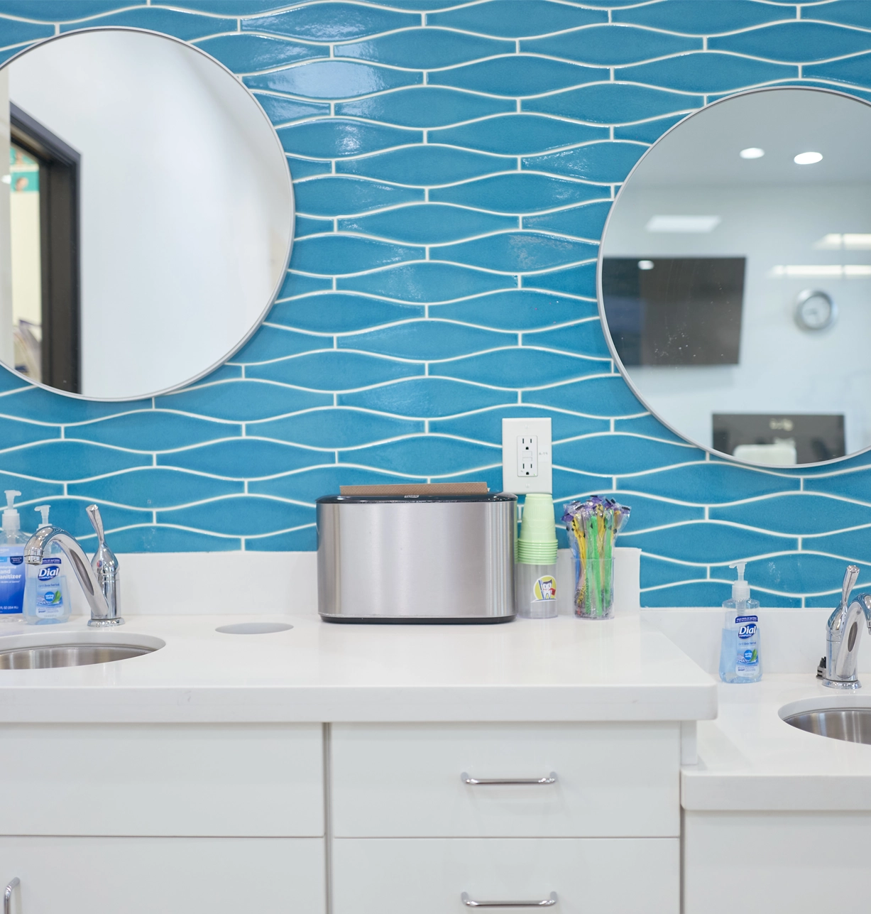 Modern pediatric dental office bathroom with blue tile backsplash, white vanity, and round mirrors.