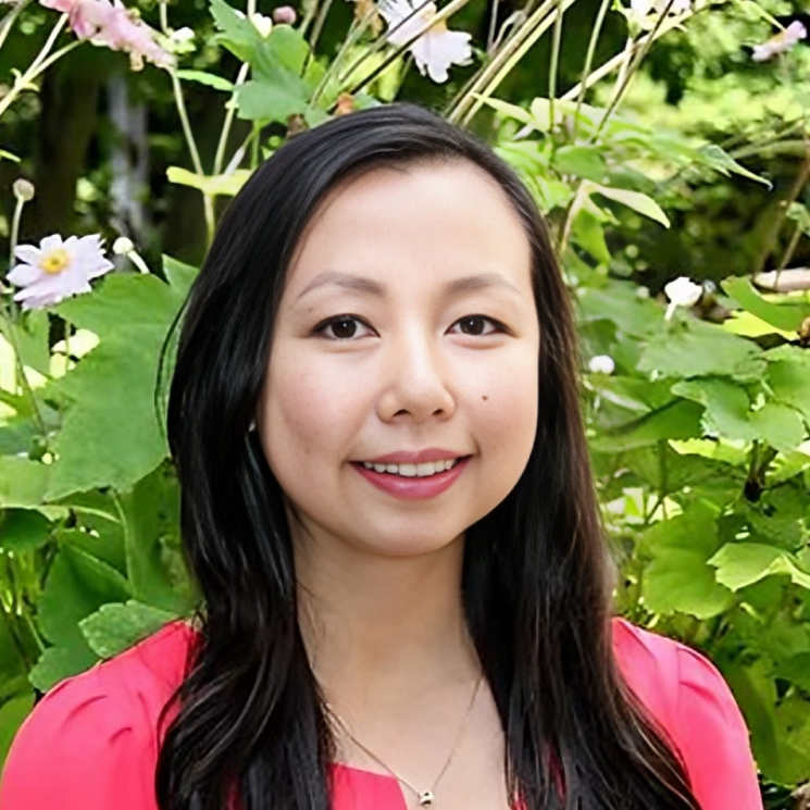 Woman smiling at camera wearing pink shirt against green foliage background