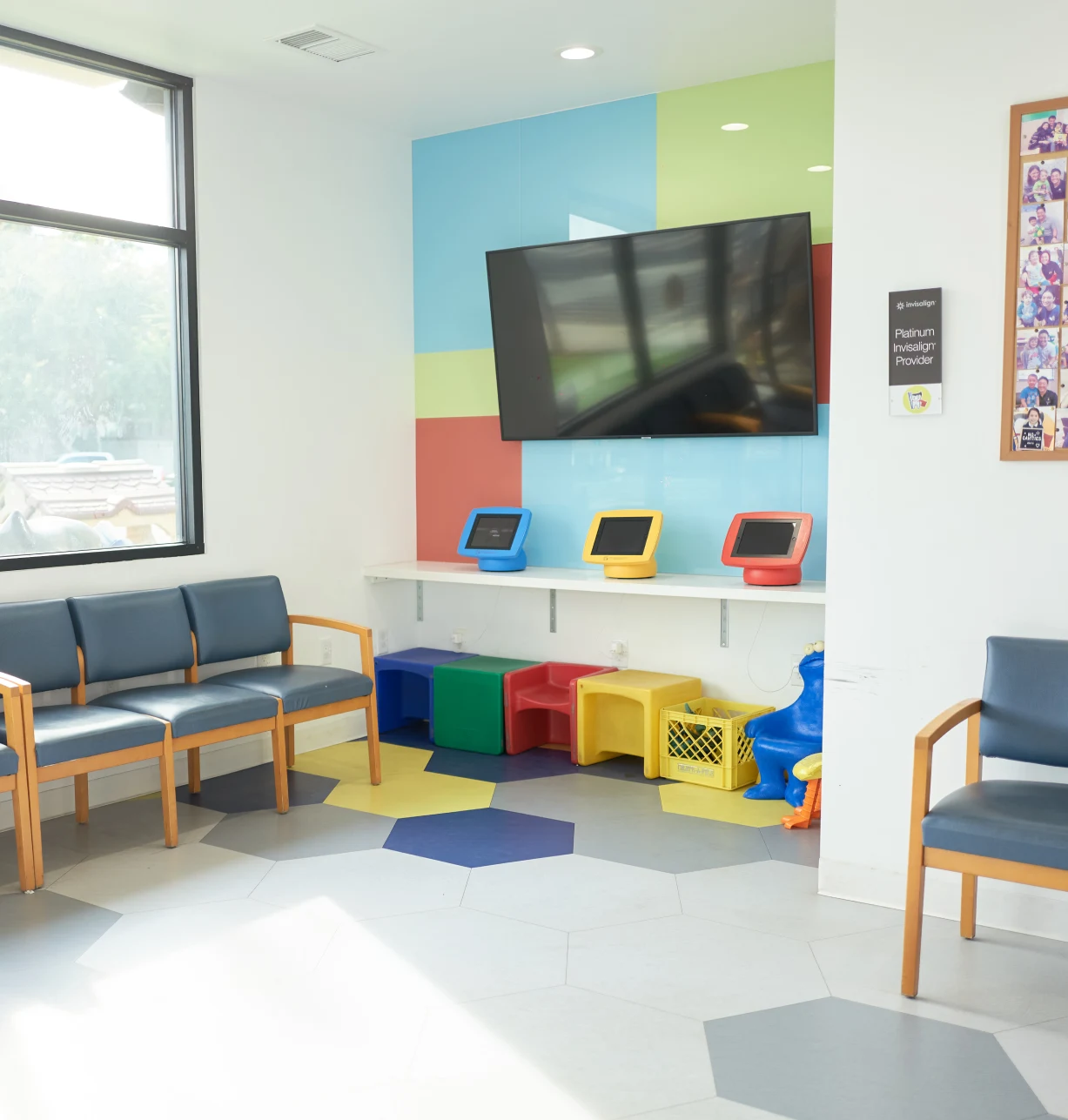 Bright pediatric waiting room with colorful storage cubes, seating, mounted TV, and child-friendly décor.