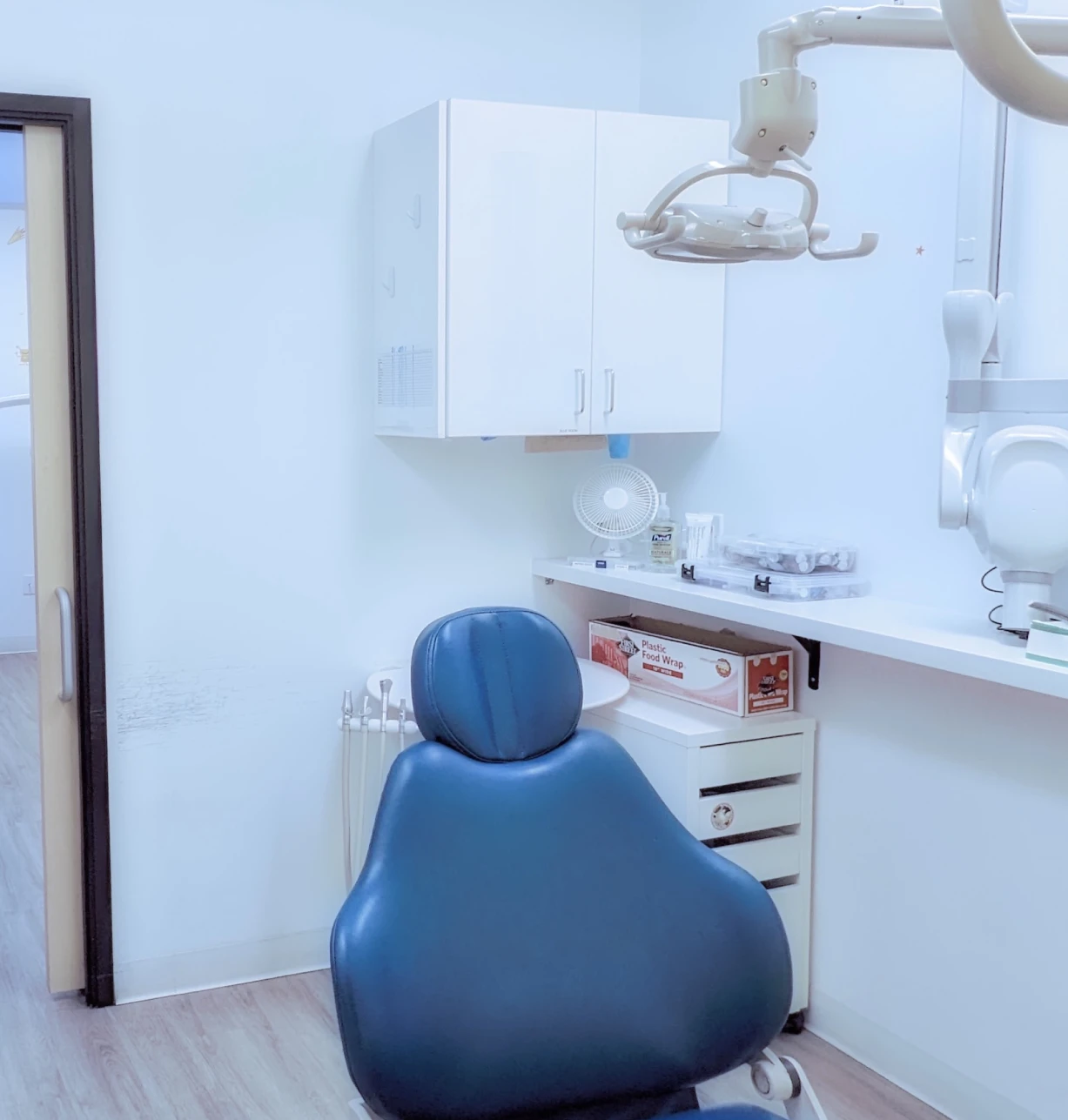 Pediatric dental patient seated in blue chair facing modern treatment station with overhead light.