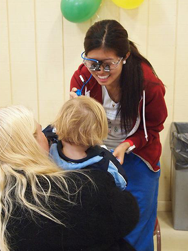 Female dentist examining young patient's teeth in bright, cheerful dental office with balloons.