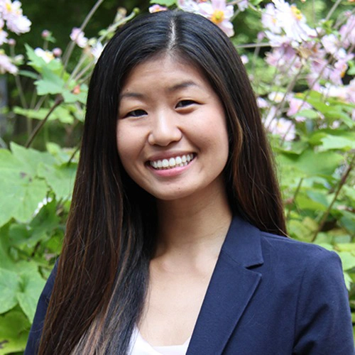 Professional portrait of smiling woman in navy blazer against flowering garden background.