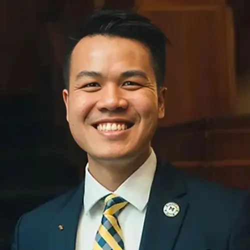 Professional headshot of smiling male dentist in navy blazer with striped tie against indoor background.