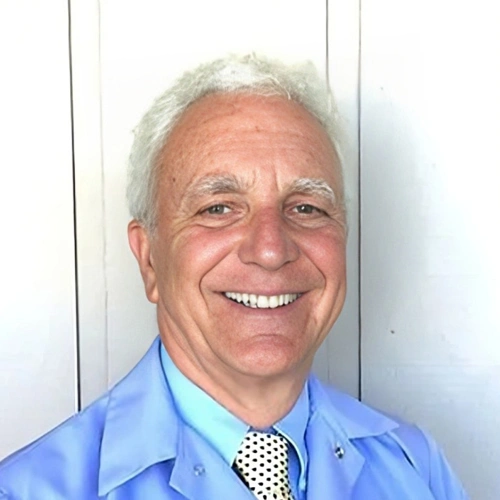 Smiling male dentist in blue shirt and polka dot tie, professional headshot for pediatric dental practice.