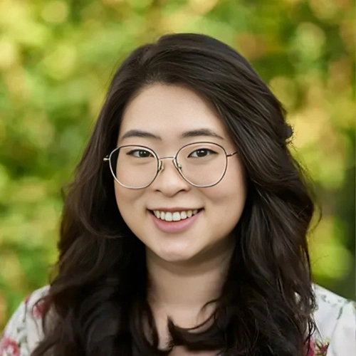 Young woman with glasses smiling at camera against green blurred background