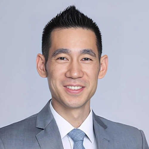Professional headshot of male dental professional in gray suit and blue tie against neutral background.