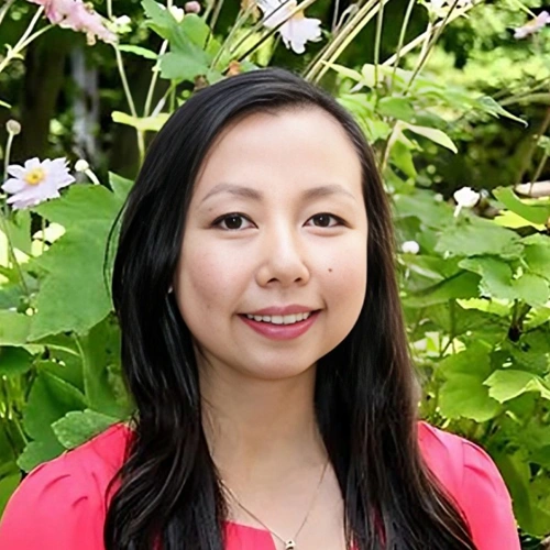 Woman smiling at camera wearing pink shirt with green foliage background