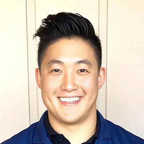 Professional headshot of smiling Asian man in dark blue shirt against neutral background.