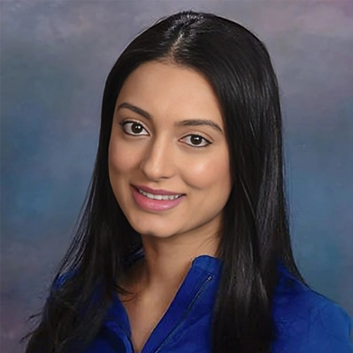 Professional headshot of woman wearing blue jacket against blue gradient background for dental practice website.