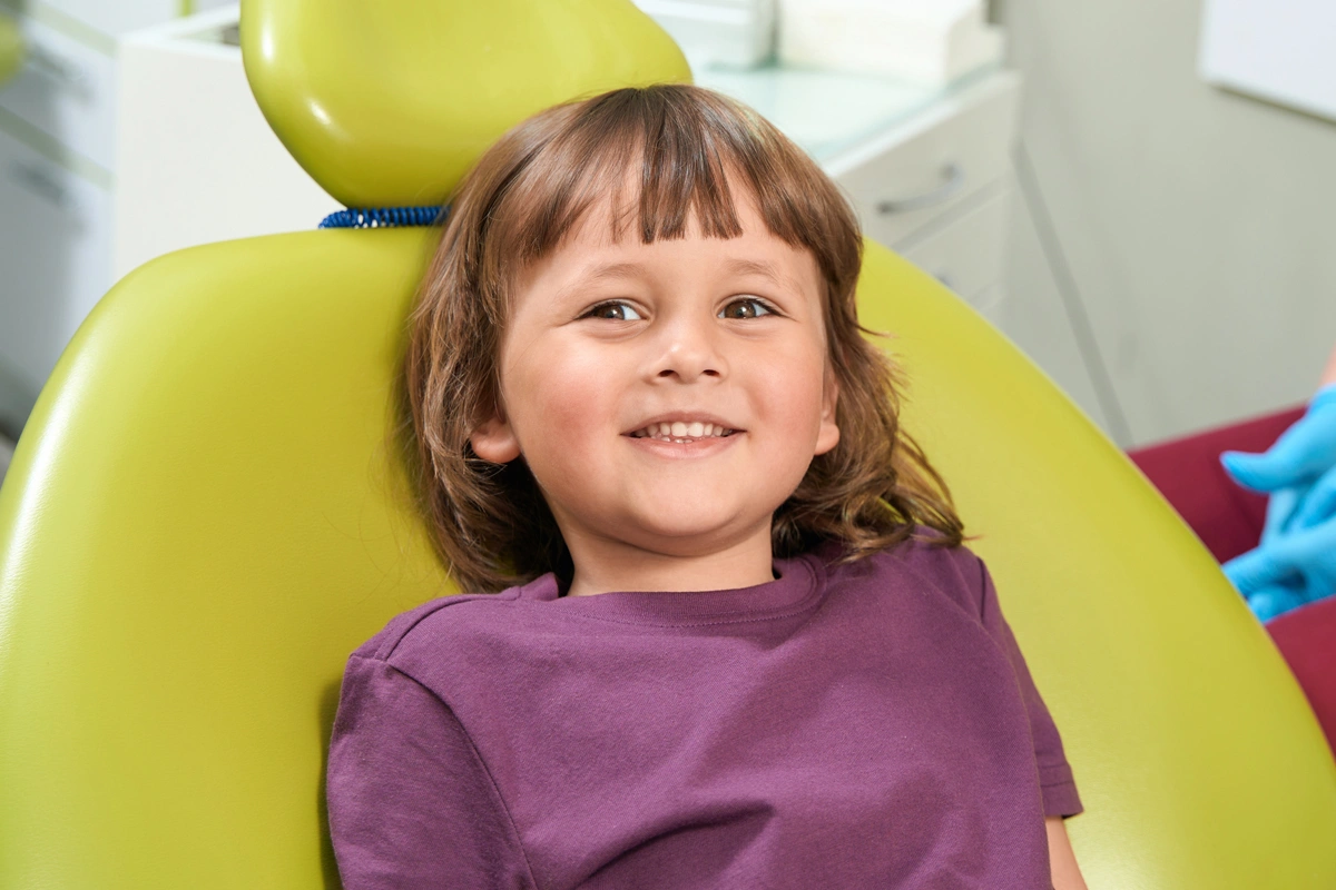 Young child smiling in dental chair at pediatric dentistry office with yellow headrest.