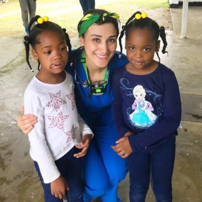 Adult in blue superhero costume poses with two smiling children wearing yellow hair accessories outdoors.