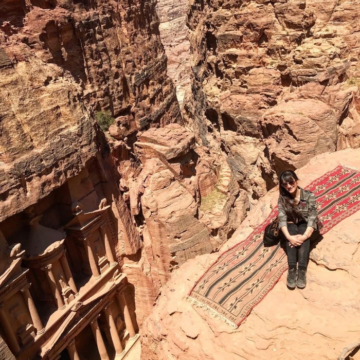 People hiking through narrow canyon with red rock walls and wooden bridge structure.